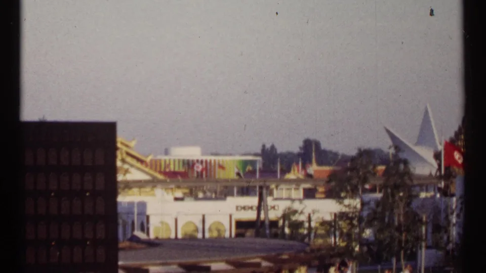 1967 Montreal Expo 67 grounds with pavilion architecture, flags, trees, and foreground structural silhouettes.