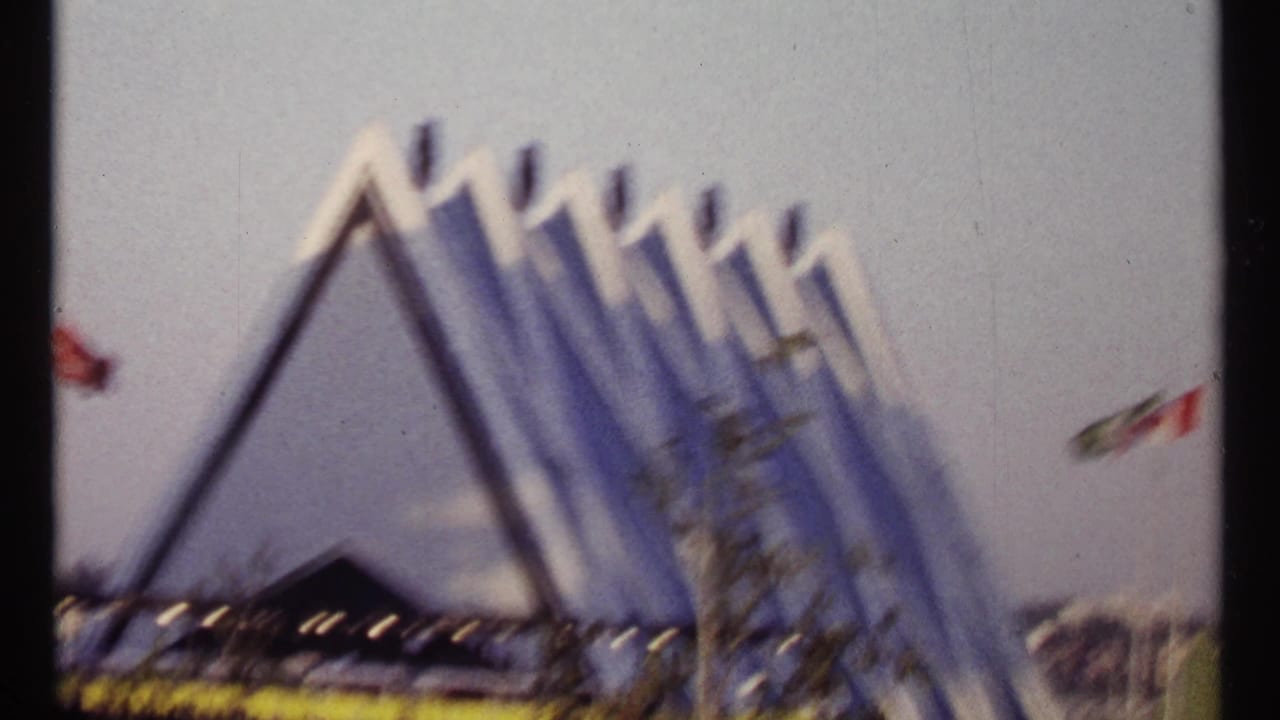 Blurred blue-and-white triangular Expo building with flags nearby.