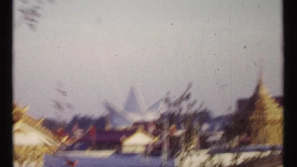 1967 Montreal fairground scene with a distant triangular structure, trees, small roofed buildings, and motion blur from passing travel.