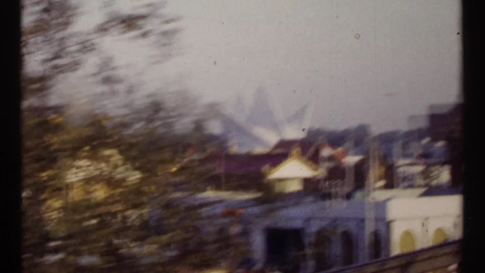 1967 Montreal drive-by view with trees and railings in the foreground and Expo-era buildings receding in the background.