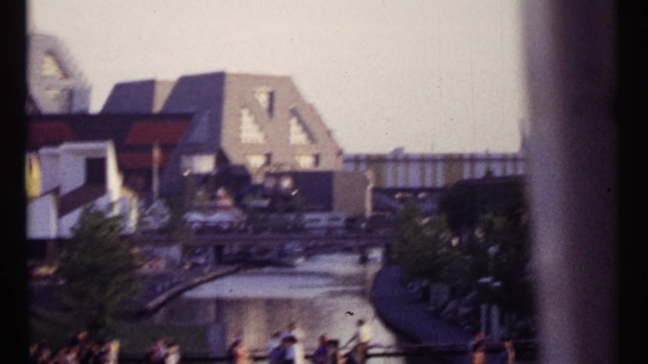 Waterway, railings, pedestrians, and angular buildings viewed through a window edge.