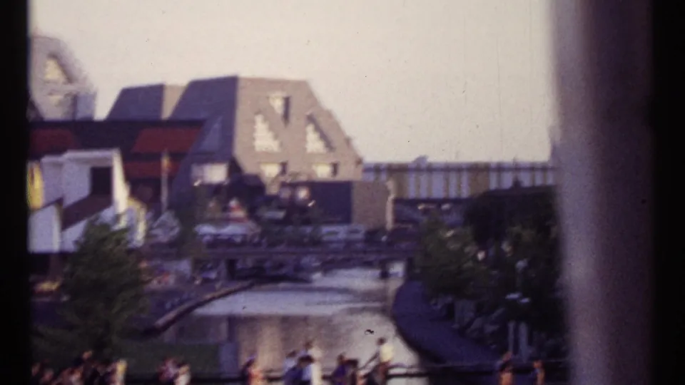 Montreal urban waterfront scene with pedestrians, railings, water, angular roofs, and a dark vertical window or frame edge.