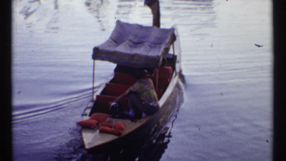A small covered boat carries passengers across calm fairground water in the 1967 Montreal World's Fair footage.