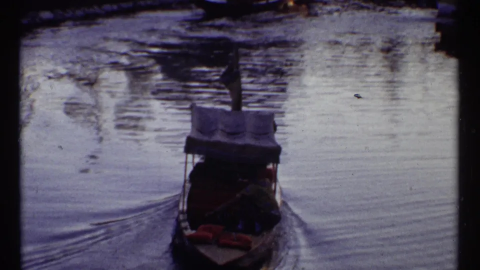 Rear view of a small canopy boat on fairground water, with Expo 67 pavilion structures and visitors in the distance.