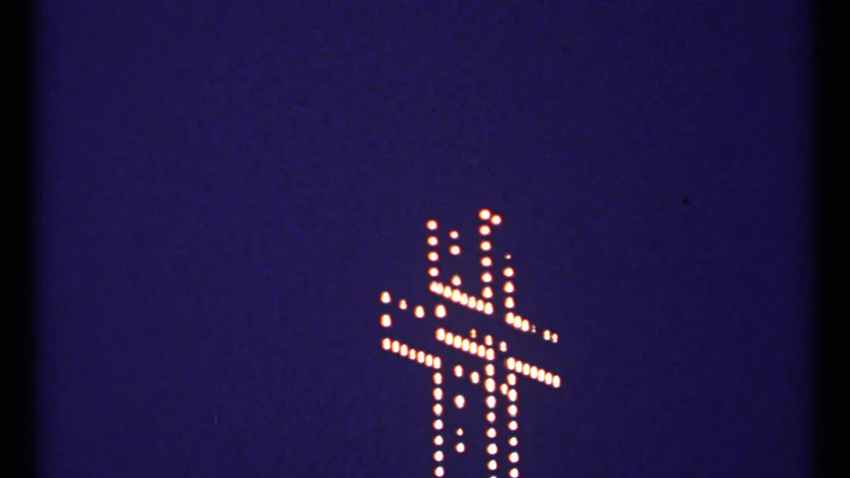 1967 Montreal 8mm frame showing the illuminated cross in warm dotted lights, framed low against a grainy blue night sky.