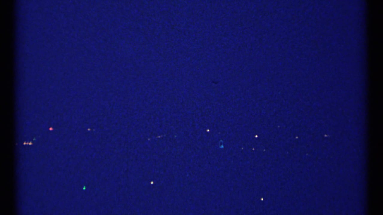 Night skyline view with small lights and a faint illuminated cross-like shape.