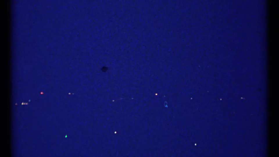 1967 Montreal home-movie frame with scattered city lights across a blue night horizon and visible 8mm frame edge.