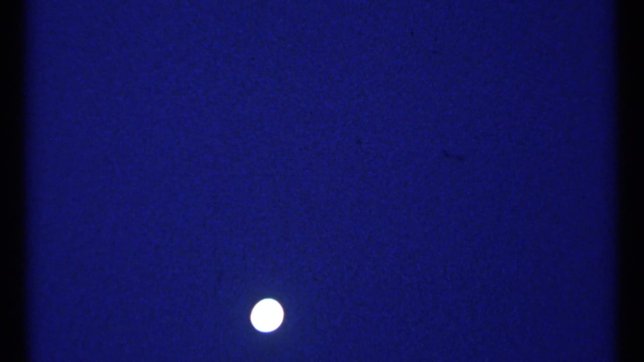 Bright moon against a deep blue night sky with dark film edges and light grain.