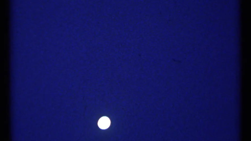 1967 Montreal 8mm frame showing a bright moon suspended in a deep blue night sky with visible film grain and edge darkness.