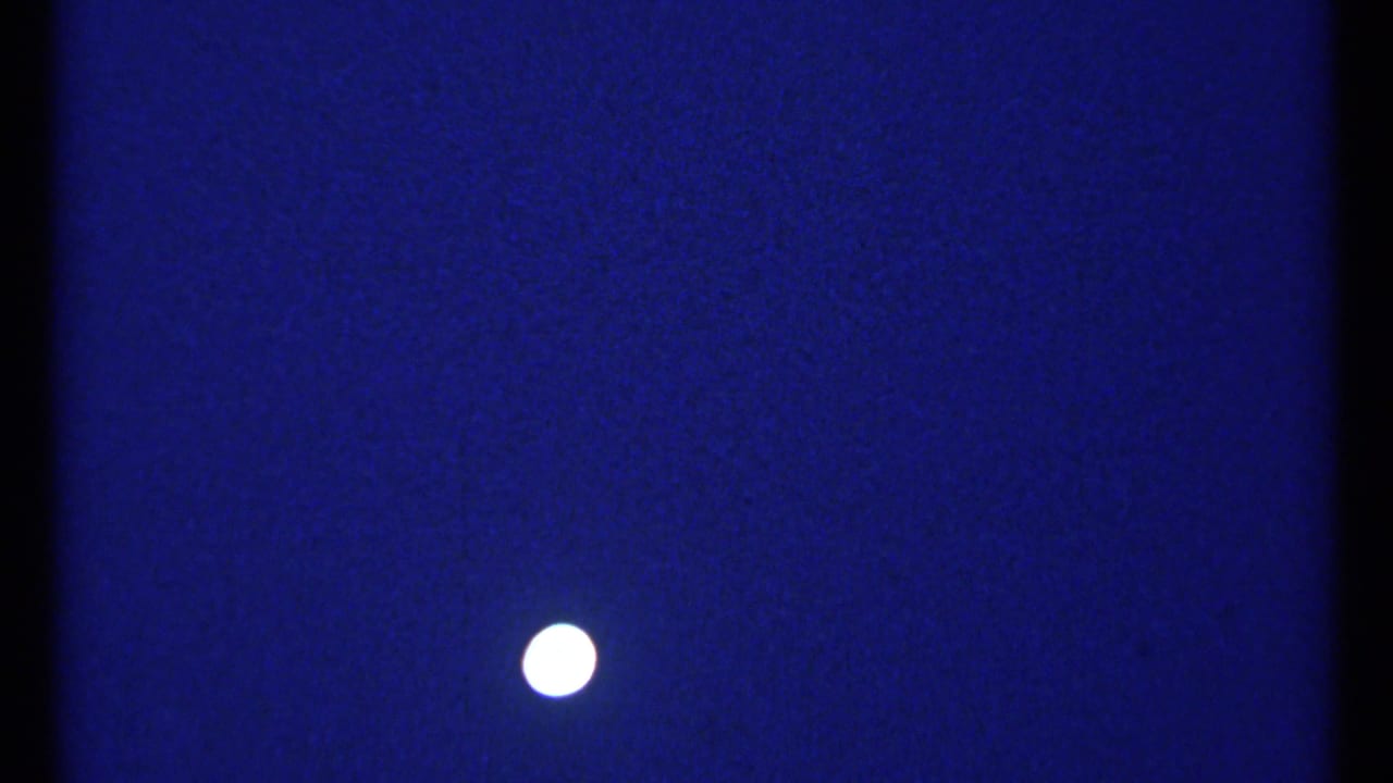 Bright moon in a blue night sky, framed by dark vertical film borders.