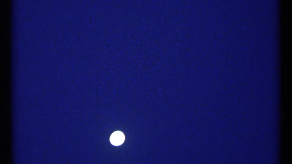 1967 Montreal 8mm frame with a small bright moon against a saturated blue night sky and visible scanned-film texture.