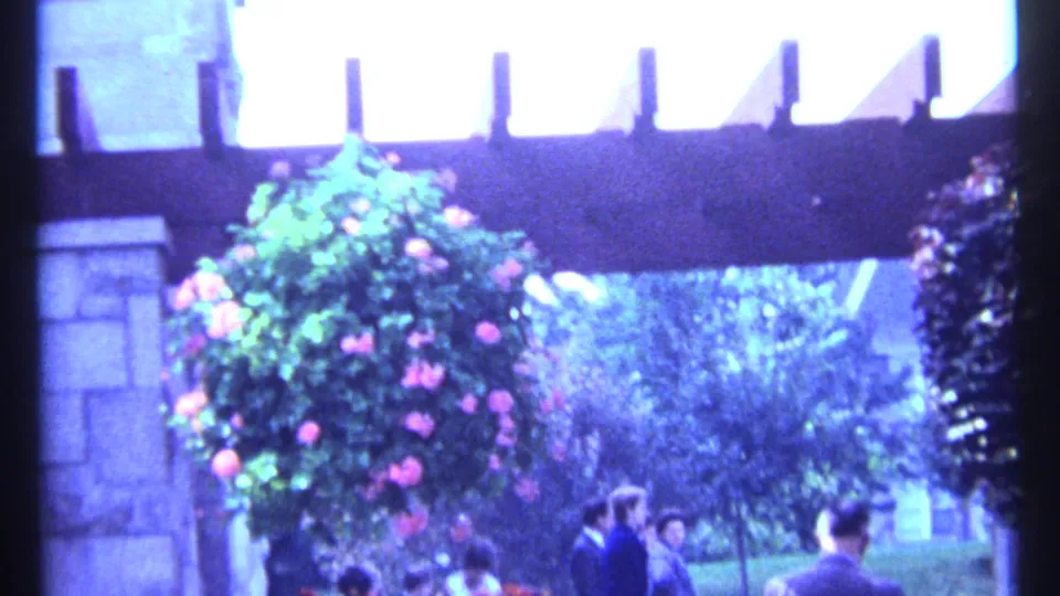 Montreal Botanical Garden entrance area with a hanging flower basket, trees, and small groups of visitors beneath the structure.