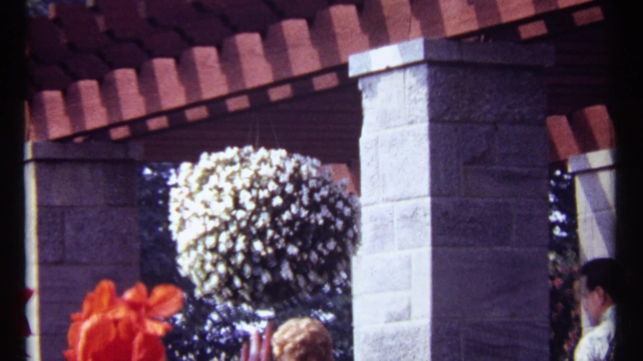 Sunlit stone patio pillars with red roof tiles and a hanging ball of white flowers.