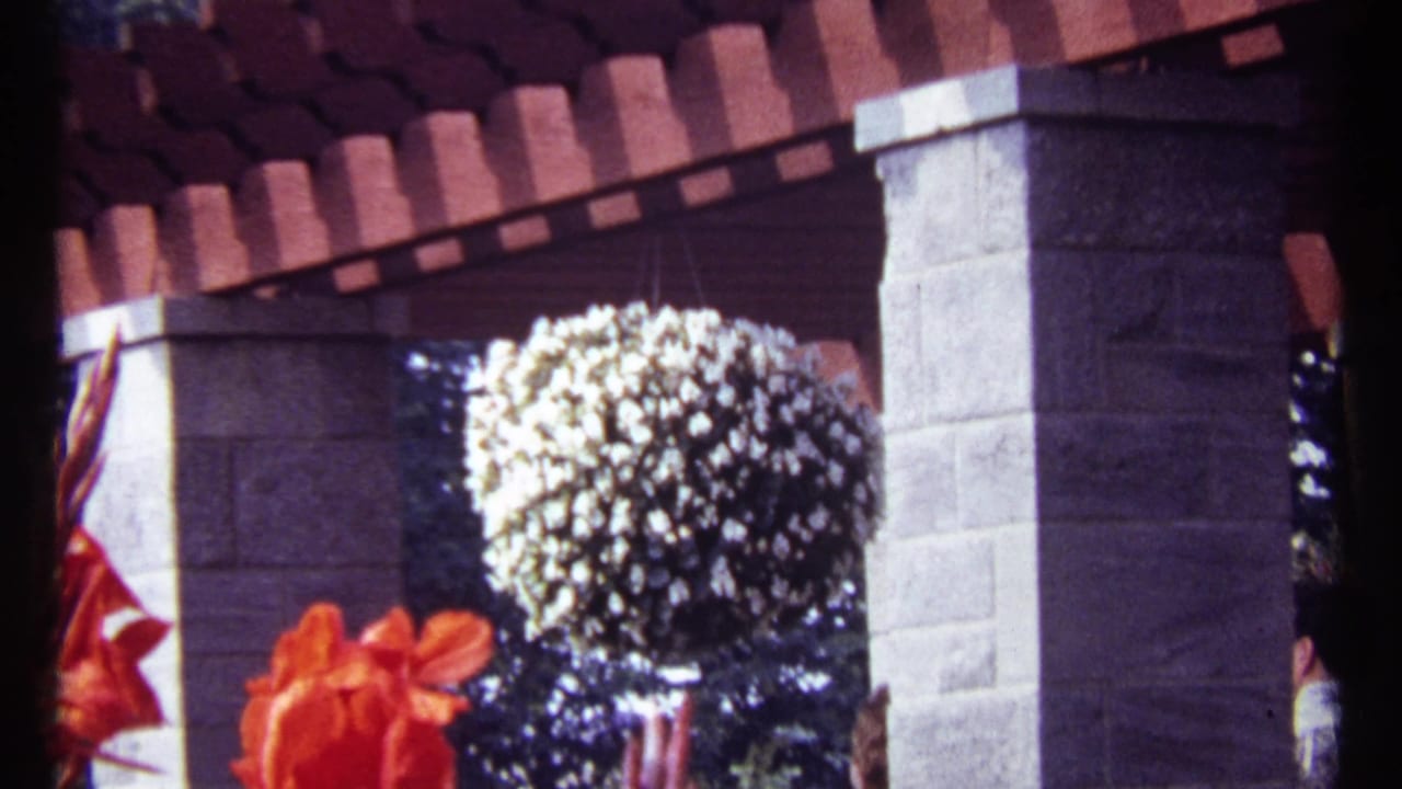 Hanging white flowers and stone patio pillars under red roof tiles with a person at the side.