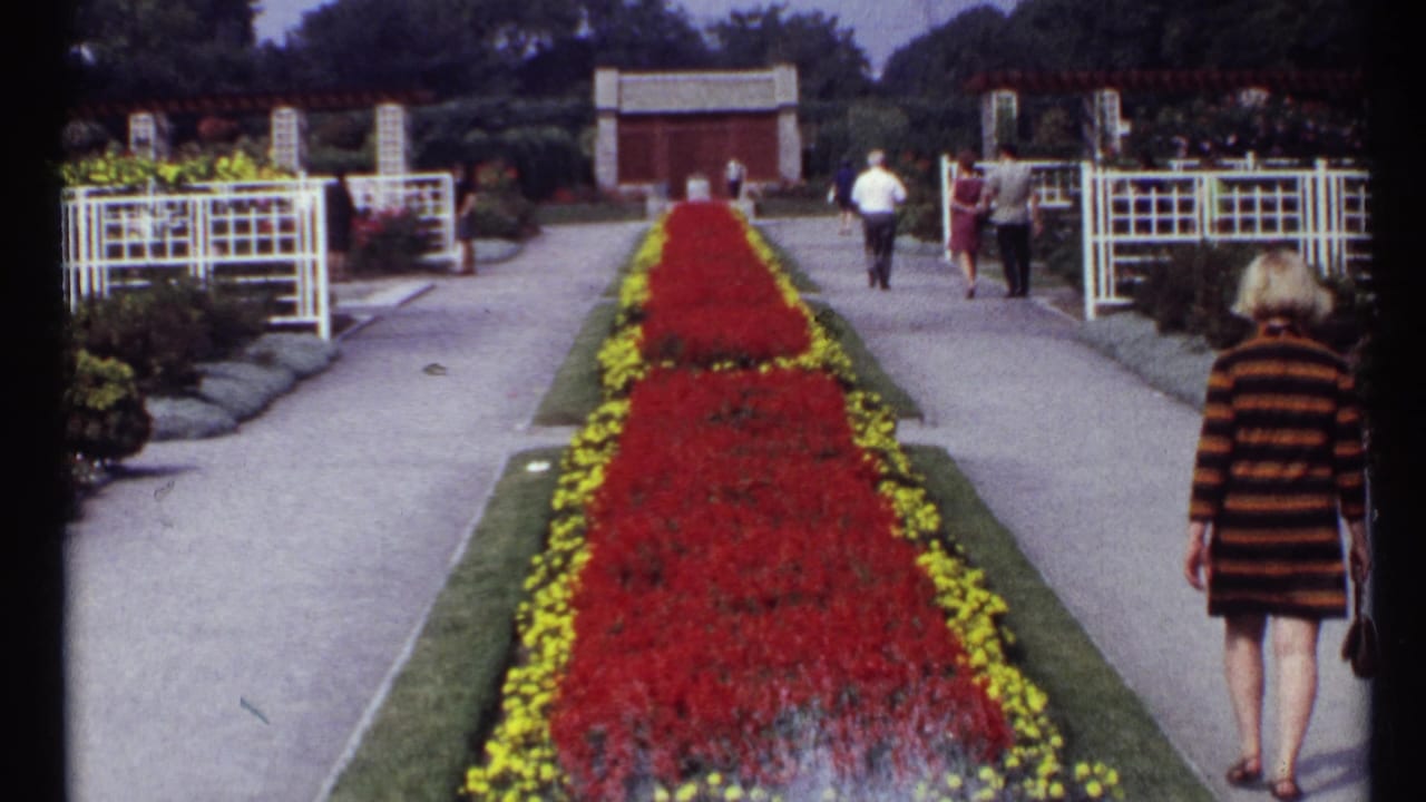Formal garden walkway with red floral median and visitors walking along paved paths.