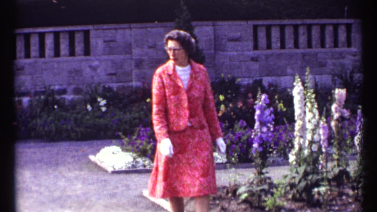Woman in red stands or walks near purple and white flowers in a garden.