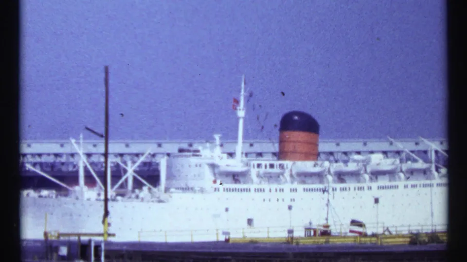 A white transatlantic-style passenger ship is docked at a Montreal port in 1967 footage, with pier structures and a dark-and-orange smokestack visible.