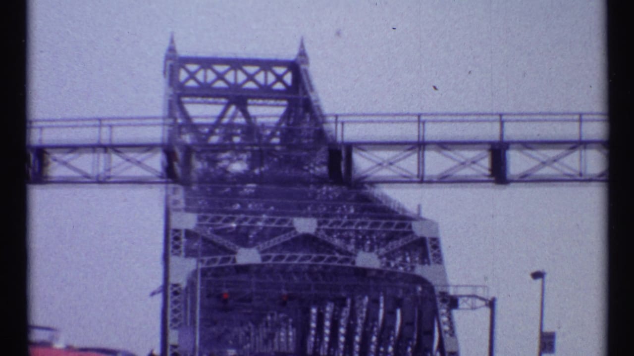 1967 Montreal bridge crossing view showing a steel lift tower, overhead walkway, traffic signal, and road lamps.