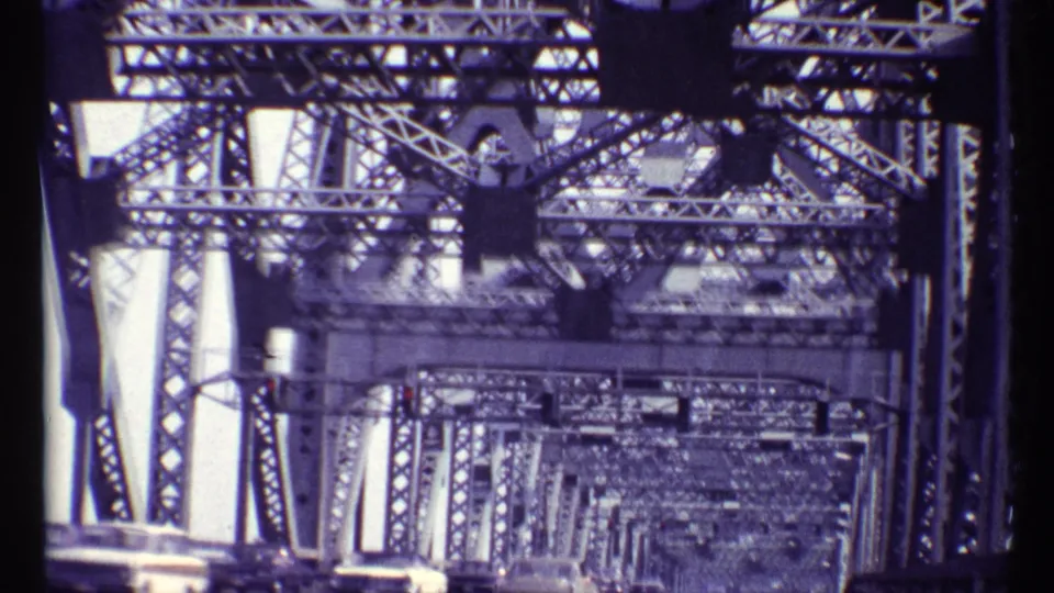 Handheld 8mm frame looking through the Alexandra Bridge truss interior, with layered beams and traffic glimpsed along the deck.