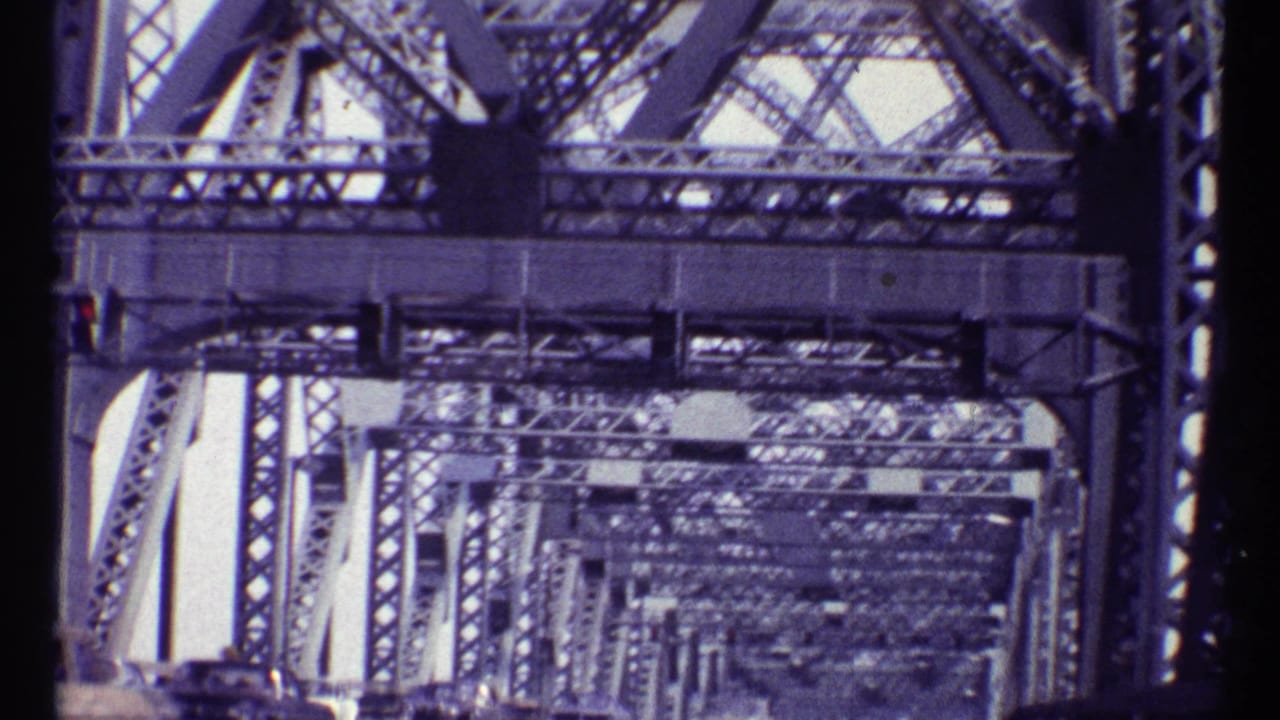 Traffic seen beneath a steel truss bridge framework.