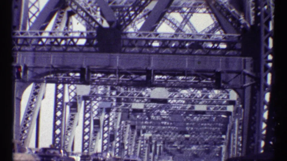 1967 Montreal bridge traffic viewed from below a dense steel truss structure, with cars moving along the roadway.