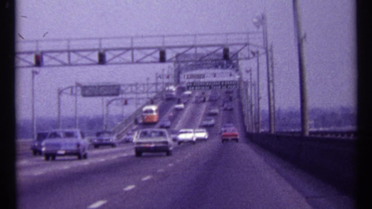 1967 Montreal roadway view with period cars moving across a bridge under overhead gantries and signs.