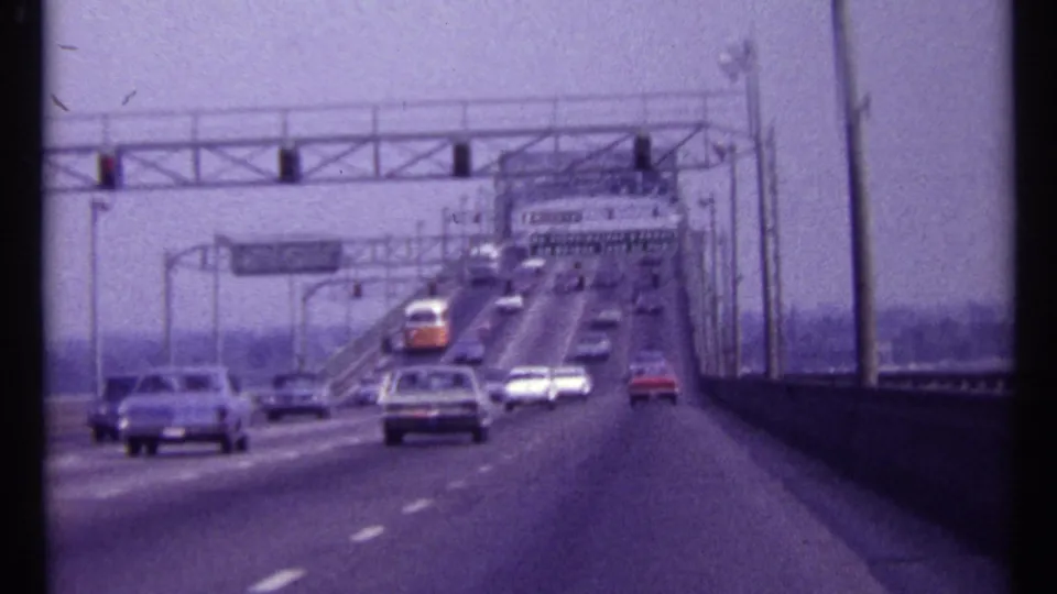 1967 Montreal roadway view with period cars moving across a bridge under overhead gantries and signs.