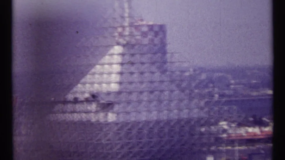 Large industrial construction frame in Montreal, filmed from a moving vehicle with parked cars and hazy skyline nearby.