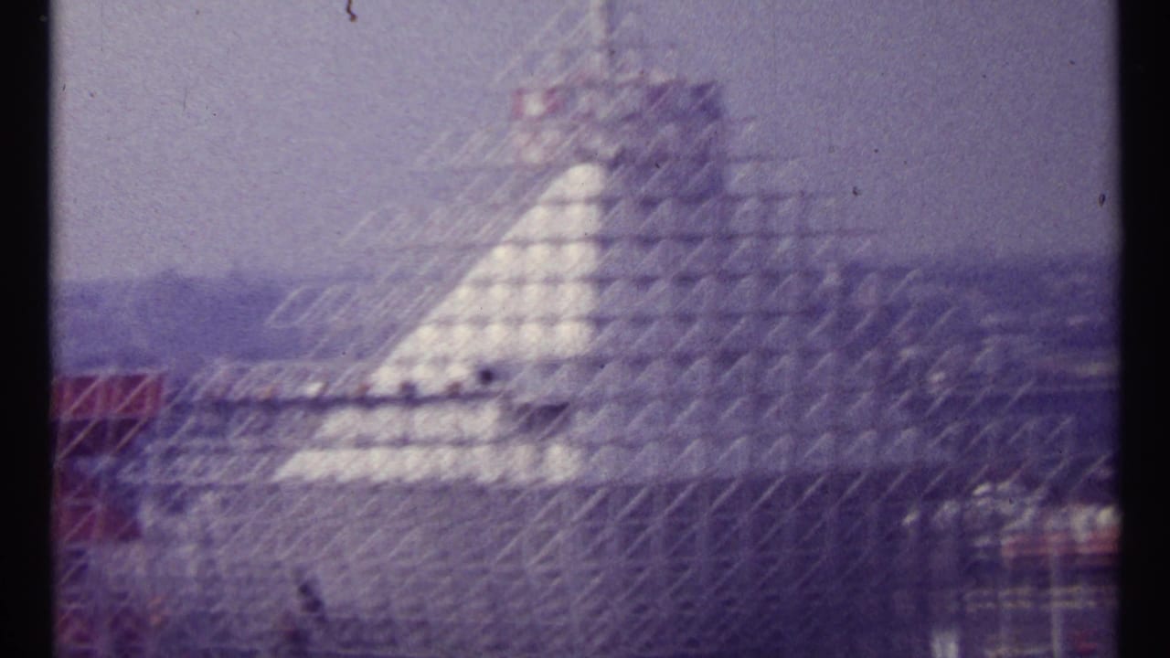 Lattice-scaffolded pale pyramid-like building under a hazy sky.