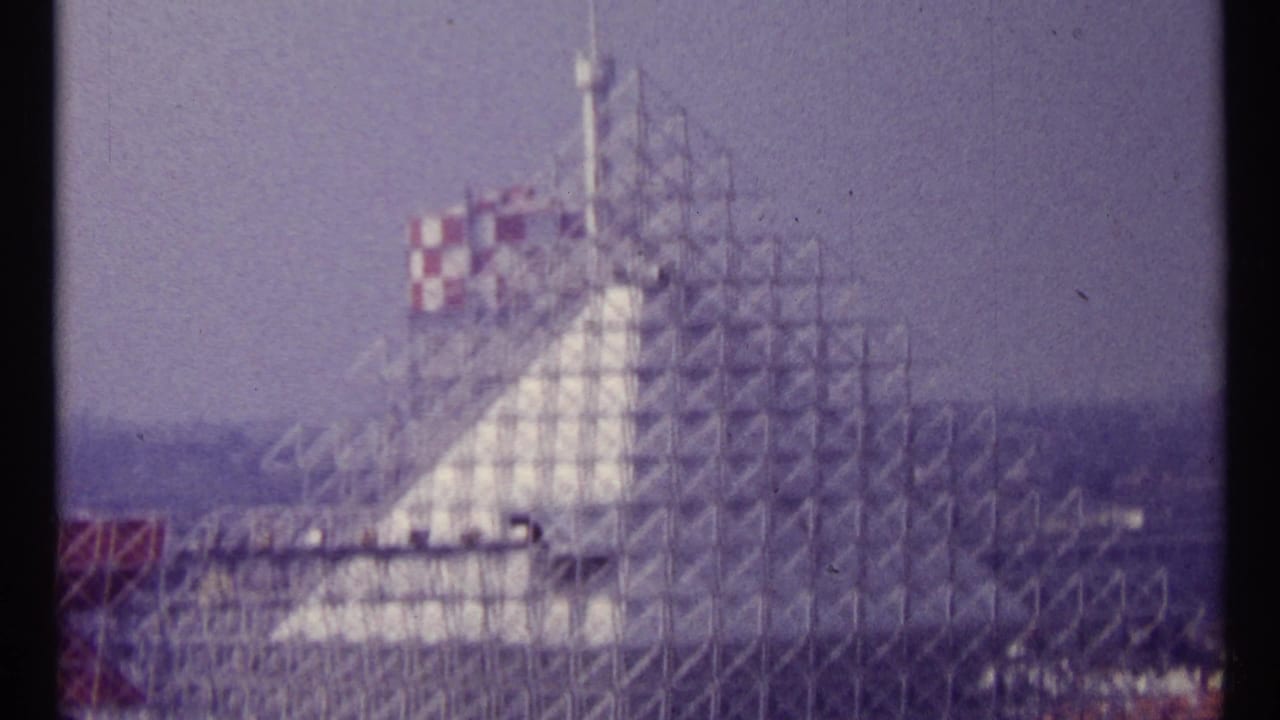 Scaffolded building with red-and-white checkered top against hazy sky.