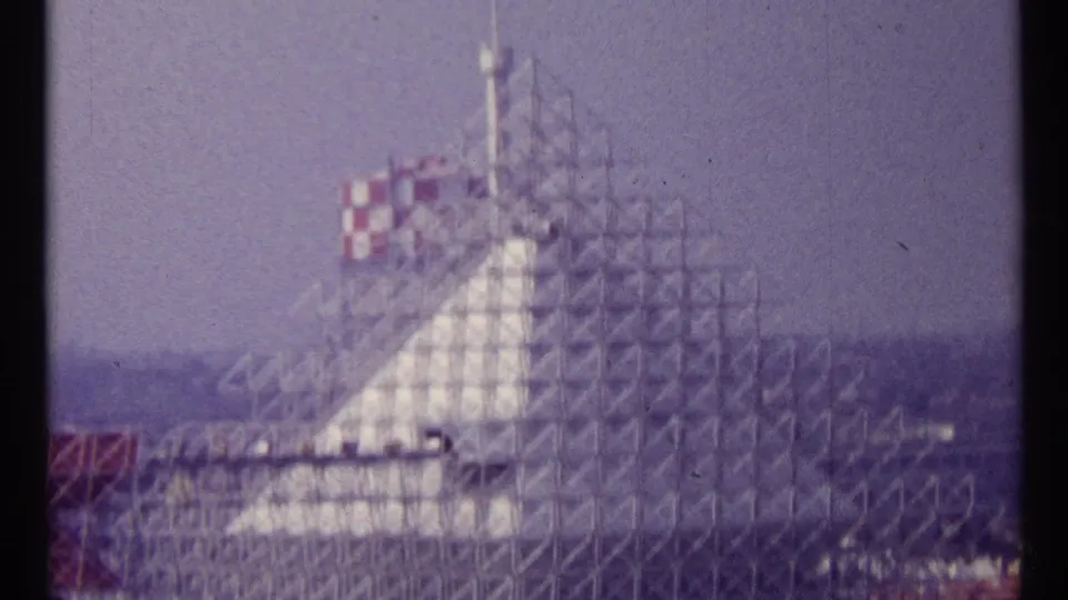 1967 Montreal frame of a lattice-wrapped pale structure with a red-and-white checkered upper section visible through soft 8mm focus.
