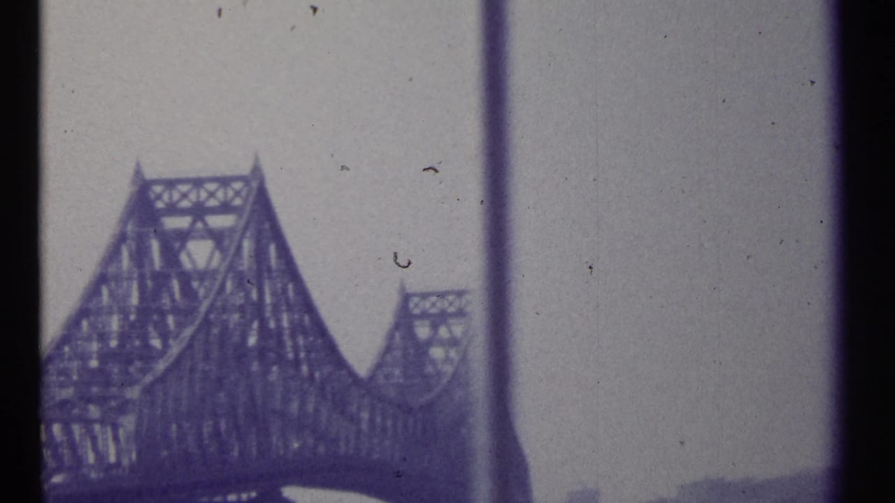 1967 Montreal-area 8mm frame showing a large steel truss bridge viewed through dark window or vehicle-frame dividers.
