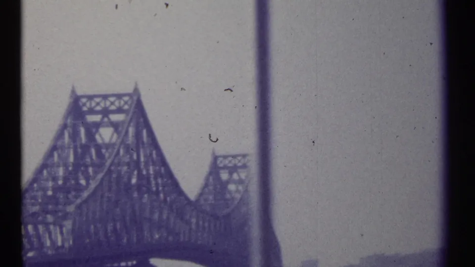 1967 Montreal-area 8mm frame showing a large steel truss bridge viewed through dark window or vehicle-frame dividers.