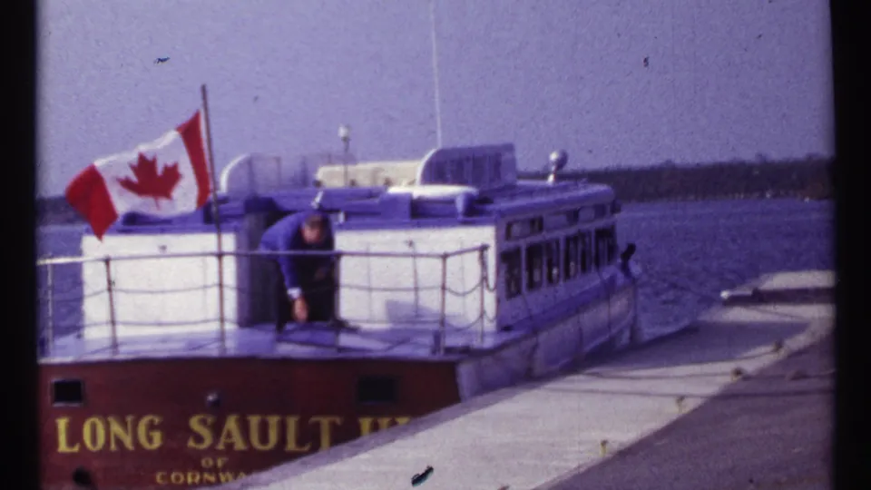 1967 Montreal frame of a Long Sault vessel at a pier, with Canadian flag and an adult man visible on deck.