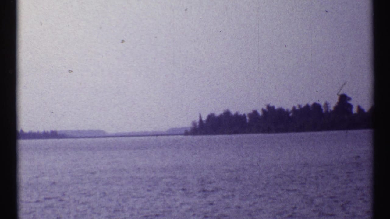 Wide lake view with a dark wooded shoreline beneath a hazy sky.