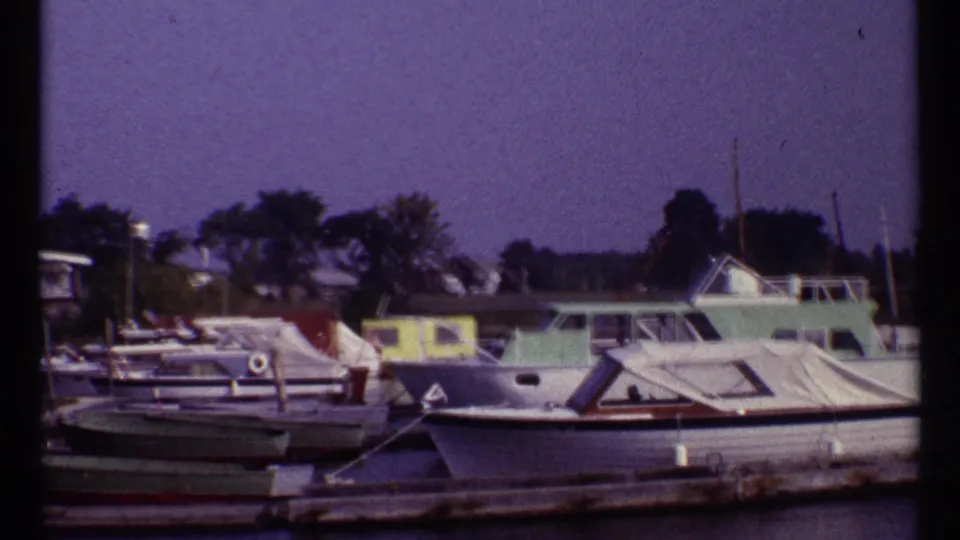 1967 Montreal marina frame showing docked boats, a wooden pier, trees, and a pale green cabin cruiser.