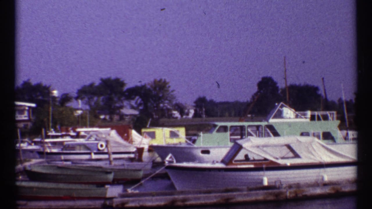 1967 Montreal home-movie frame showing cabin cruisers and covered boats tied along a wooden harbor dock.