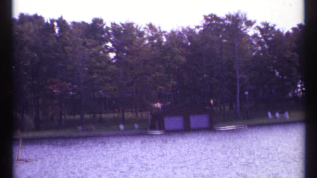 Wooded lakeshore with a small boathouse across rippled water.