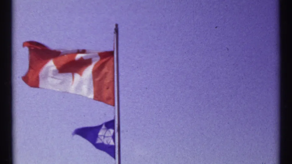 Canadian flag and a blue flag wave on a pole in a purple-tinged 8mm frame from the Montreal home movie.