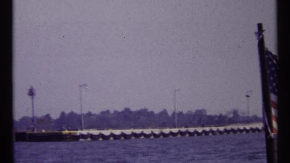 Wide 1967 Montreal waterfront view showing a long pier, repeated lampposts, water, and an American flag partly visible at right.