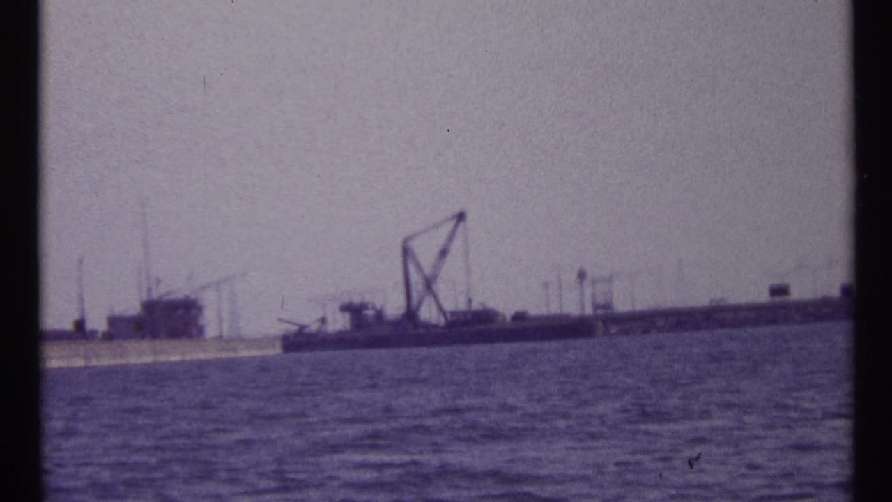 1967 Montreal waterfront view showing rippled water, a moored barge, crane structure, and distant industrial features.