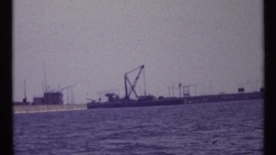 1967 Montreal waterfront view showing rippled water, a moored barge, crane structure, and distant industrial features.