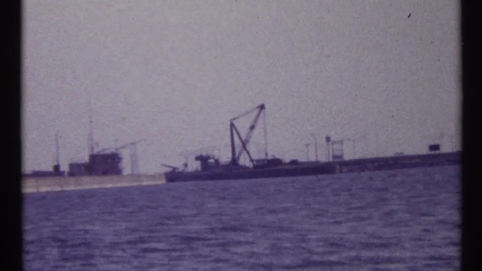 1967 Montreal waterfront frame with a barge, tall crane structure, low pier, and industrial shoreline across the water.