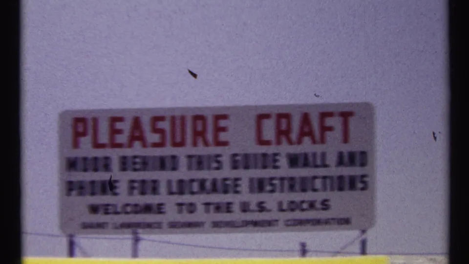 1967 Montreal home-movie frame showing a readable pleasure craft sign welcoming boats to the U.S. Locks.