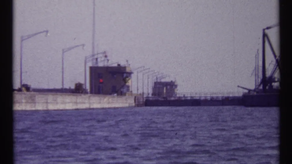 1967 Montreal waterway view with lock structures, control buildings, railings, and a crane barge across rippling water.