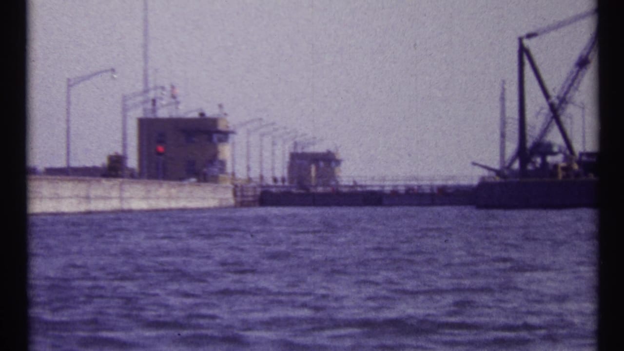 Waterfront lock structure with small buildings, a red signal light, and crane equipment on the right.