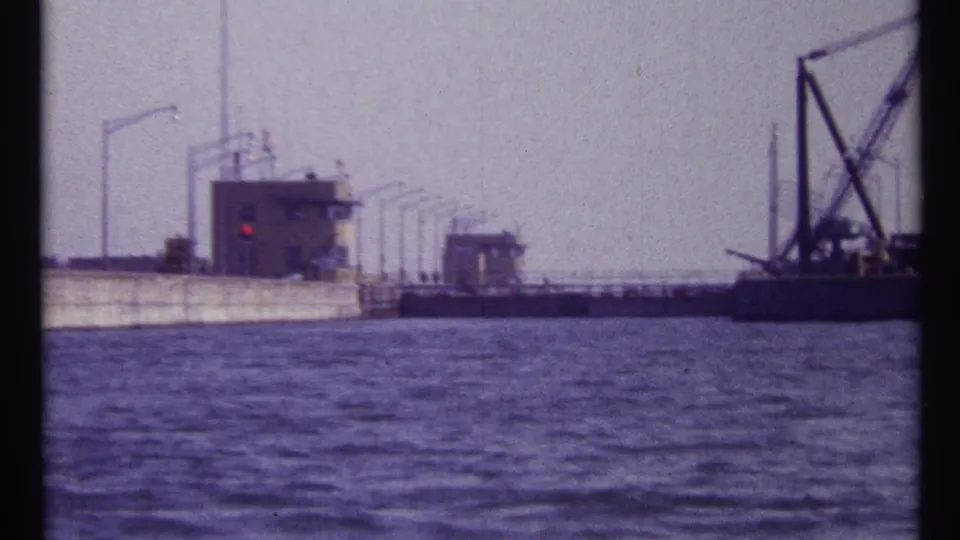 1967 Montreal waterway view with a concrete lock or dam, control buildings, a red signal light, and crane equipment near the right edge.