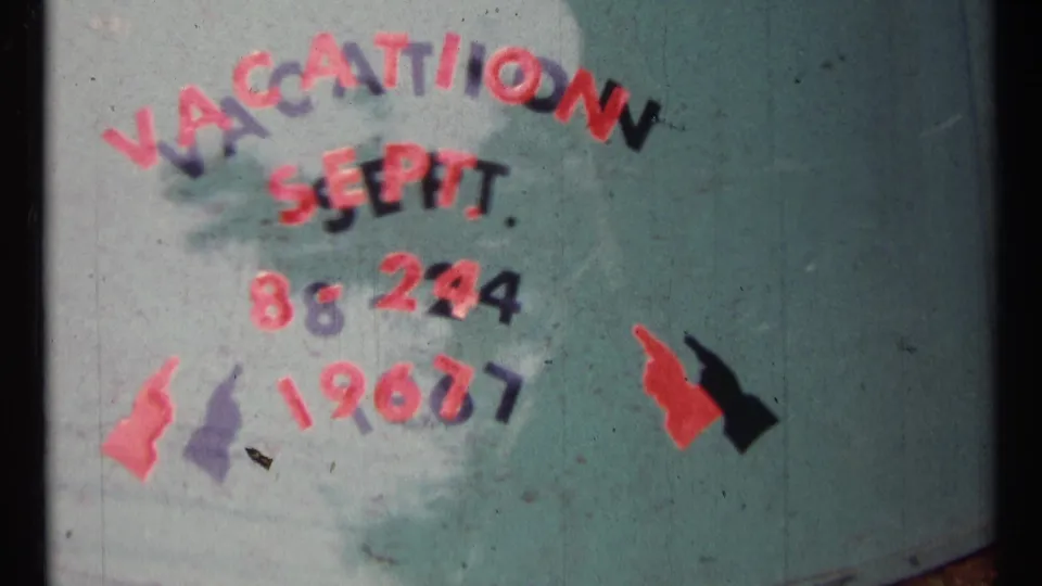 Close view of the 1967 vacation title card, with red letters and black shadows painted on a teal window or surface.