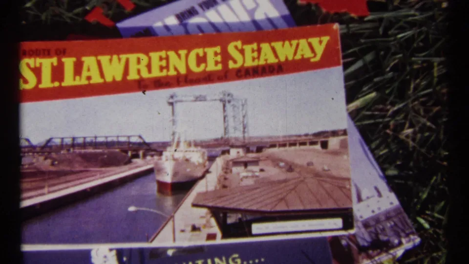 1967 Ottawa home-movie frame with a St. Lawrence Seaway brochure and a partial Quebec pamphlet arranged on grass.