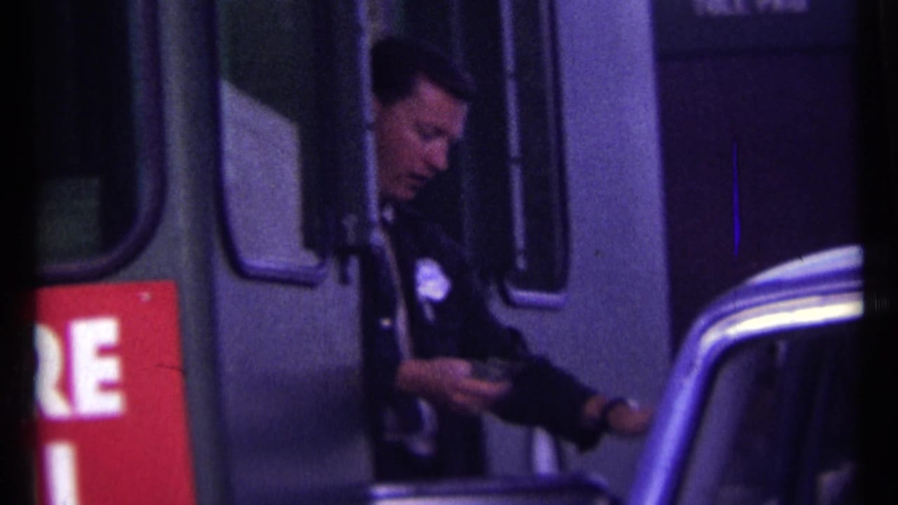 Police officer stands at a toll booth beside a car, holding money near a red toll sign.